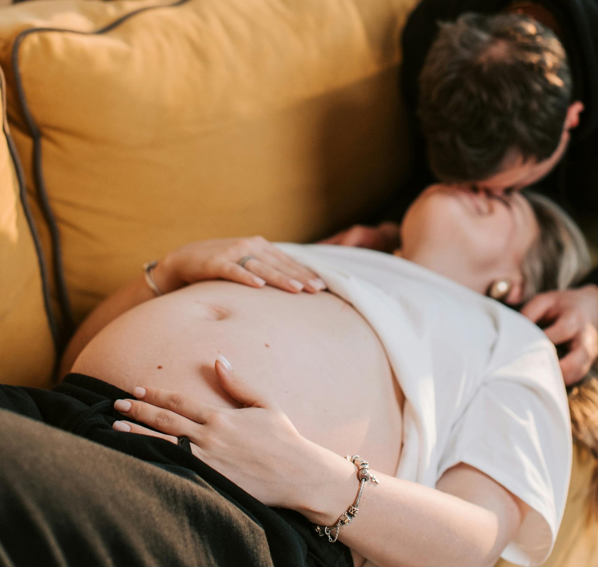 A pregnant woman lying down as her partner kisses her | Source: Pexels