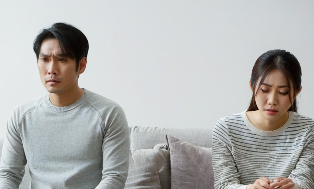 An unhappy couple sitting at a distance on the sofa | Source: Midjourney