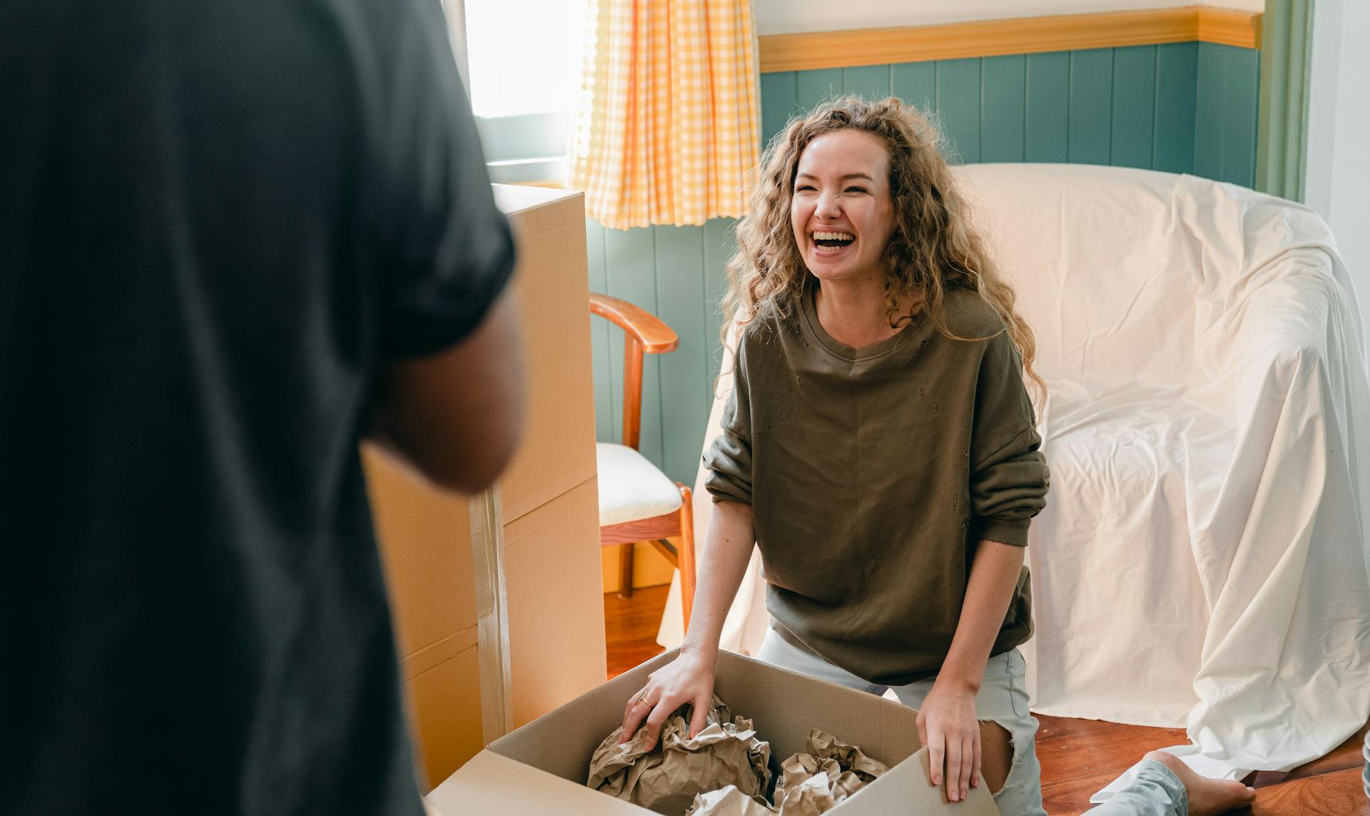 A woman sitting near a box of clothes laughing while looking at her husband | Source: Pexels